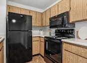 Thumbnail 27 of 31 - Kitchen in 2 bed 2 Bath Bent Tree apartment with wood plank-style flooring, light wood cabinets, black appliances, and plenty of storage for all of your needs!