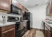 Thumbnail 13 of 31 - Kitchen in 2 Bedroom 1 Bath Option B Bent Tree Apartment with wood plank-style flooring, dark wood cabinets, black appliances, and modern marbled countertop.