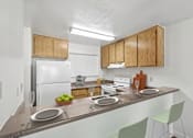 Thumbnail 27 of 37 - Kitchen with bar top seating in 1 Bed 1 Bath B apartment home at California Place apartments with light wood cabinetry and white appliances