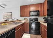 Thumbnail 21 of 37 - Kitchen in 2 Bedroom California Place apartment with wood-style plank flooring, dark wood cabinetry, and black appliances. Plenty of storage space for all of your needs!