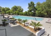 Thumbnail 24 of 69 - a swimming pool with tables and chairs and trees in the background at The Venue at Orange Apartments, Redlands, California