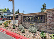 Thumbnail 2 of 31 - Entrance to Bent Tree Apartments with stone monument sign and large trees providing a cozy atmosphere