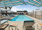 Thumbnail 9 of 38 - Swimming pool with striped shade umbrellas and lounge chairs at Altitude Apartments, Moreno Valley, California