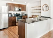 Thumbnail 2 of 17 - A modern kitchen with a refrigerator, microwave, oven, sink, and wooden cabinets.