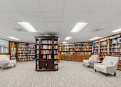 Thumbnail 12 of 37 - A library with bookshelves and chairs at Hampton Apartments, Clearwater, FL