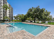 Thumbnail 11 of 37 - A swimming pool surrounded by a brick patio and lounge chairs at Hampton Apartments, Clearwater, FL, 33759
