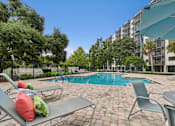Thumbnail 8 of 37 - A pool surrounded by chairs and trees with a building in the background at Hampton Apartments, Clearwater
