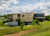 Thumbnail 66 of 112 - A modern building with a flat roof and large windows is surrounded by a grassy area with trees at The Residences at Tesson Ridge Apartments, Saint Louis, MO