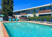 Thumbnail 28 of 31 - a swimming pool with blue chairs and a building in the background