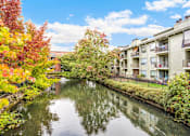 Thumbnail 25 of 27 - A canal with buildings on the side and trees with red leaves.
