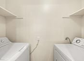 Thumbnail 24 of 27 - Two white washing machines in a laundry room.