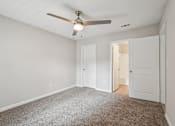 Thumbnail 31 of 40 - A room with a ceiling fan and carpeted floor.