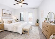 Thumbnail 11 of 25 - 3-Bedroom Apartments in Churchill Estates, TX - Apex Apartments - Bedroom With White Bedding, Wood Furniture, A Ceiling Fan, Soft Area Rug, And Glass Door.