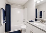 Thumbnail 18 of 40 - A bathroom with a white toilet, a white sink, and a white bathtub with a blue shower curtain.