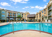 Thumbnail 1 of 24 - Apartments for Rent in Converse, TX - The Heights at Converse - Resort-Style Swimming Pool With Lounge Seating, Covered Cabana, Wooden Pergolas, Metal Fence, and Apartment Buildings.