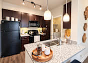 Thumbnail 10 of 30 - A kitchen with a black fridge and a granite counter top.