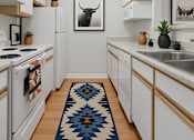Thumbnail 16 of 26 - A kitchen with white cabinets and a blue rug on the floor.