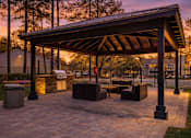 Thumbnail 38 of 40 - A pavilion with a stone floor and a roof is surrounded by trees.