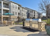 Thumbnail 21 of 27 - a patio with a grill and a table and chairs in front of an apartment building