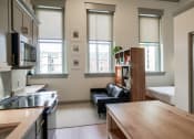 Thumbnail 14 of 22 - Kitchen island and living room with 3 large windows in apartment at Myers Medical Lofts