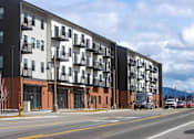 Thumbnail 1 of 18 - A modern apartment building with balconies and a parking lot in front.