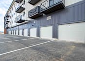 Thumbnail 3 of 18 - A parking lot in front of a grey building with a balcony on the second floor.