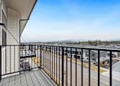 Thumbnail 12 of 18 - A balcony with a black railing and a view of a parking lot and distant trees.