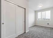 Thumbnail 17 of 18 - A room with a carpeted floor and a window with a view of buildings outside.