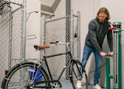 Thumbnail 14 of 24 - A man is leaning on a green machine while holding a bicycle.