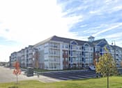 Thumbnail 24 of 34 - A large apartment complex with a parking lot in front.