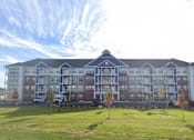 Thumbnail 25 of 34 - A large building with a grassy area in front of it.
