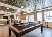 Thumbnail 6 of 34 - A pool table is in the middle of a room with a bar and a kitchen in the background.