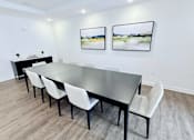 Thumbnail 12 of 34 - A long black table with white chairs in a room with two pictures on the wall.