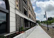 Thumbnail 11 of 34 - A sidewalk runs alongside a building with a brick facade and a street lamp.