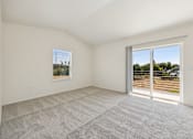 Thumbnail 35 of 74 - A room with a carpeted floor and a sliding glass door leading to a parking lot.