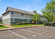 Thumbnail 11 of 35 - A parking lot in front of a two-story building with a green lawn and trees.