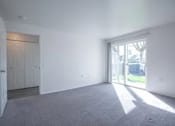 Thumbnail 26 of 34 - A large empty room with a carpeted floor and a sliding glass door leading outside.
