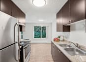 Thumbnail 23 of 44 - A kitchen with a stainless steel refrigerator and a window with greenery outside.