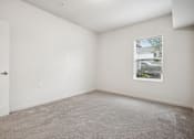 Thumbnail 21 of 46 - A room with a carpeted floor, a door, and a window with a view of a building outside.