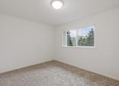 Thumbnail 20 of 36 - A room with a carpeted floor and a window showing a view of a house and trees.