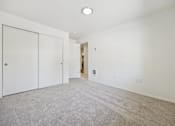 Thumbnail 23 of 37 - A room with white walls and a carpeted floor with a white door on the left and a white closet door on the right.