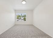 Thumbnail 53 of 74 - A room with a carpet floor and a window showing trees outside.