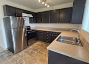 Thumbnail 2 of 17 - A kitchen with a stainless steel refrigerator and black cabinets.