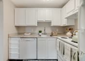 Thumbnail 26 of 31 - A white kitchen with a sink, dishwasher, and oven.