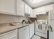Thumbnail 25 of 31 - A white kitchen with a refrigerator, oven, and sink.