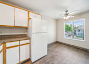 Thumbnail 24 of 35 - A white refrigerator in a kitchen with wooden cabinets.