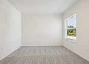 Thumbnail 58 of 74 - A room with a carpeted floor and a window showing a view of trees and a building outside.