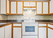 Thumbnail 25 of 35 - A white stove is in a kitchen with wooden cabinets.