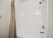 Thumbnail 29 of 74 - A white bathtub with a shower head and a curtain hanging on the side.