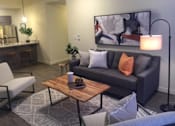 Thumbnail 34 of 46 - A modern living room with a grey couch, a wooden coffee table, and a large painting on the wall.